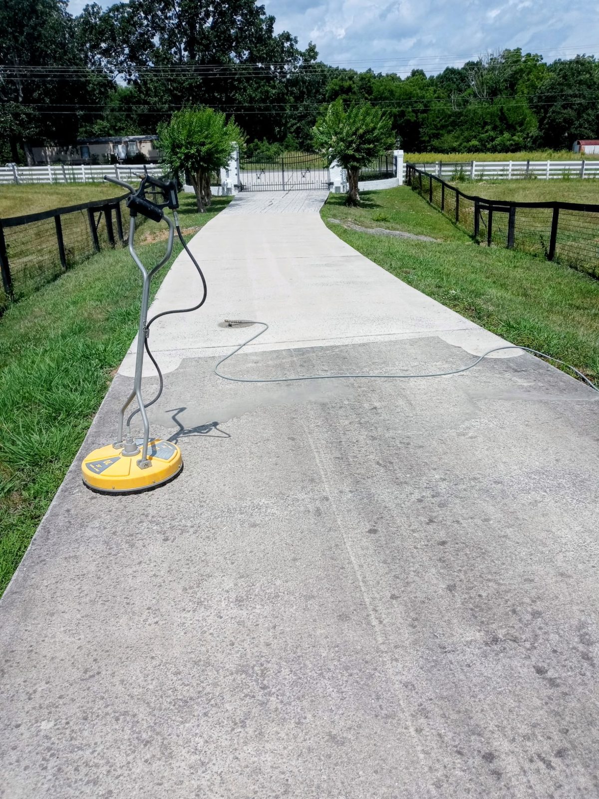 Long concrete driveway half pressure-washed with a surface cleaner showing the clean line